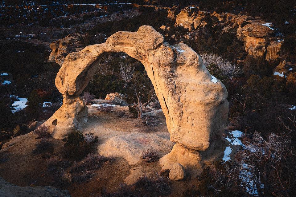 Golden light illuminates the arch and the surrounding sandstone features.